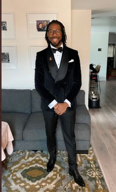 a man in a tuxedo is sitting on a couch and smiling at the camera