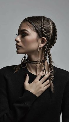 a woman with braids and rings on her neck wearing a black sweater, standing in front of a gray background