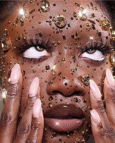 a woman with her hands on her face and eyes covered in gold glitters, looking at the camera