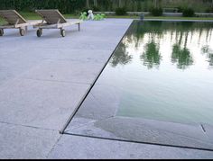 two lawn chairs sitting on top of a cement patio next to a pool with water