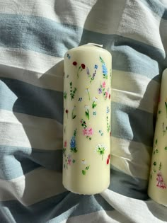 two candles are sitting on a bed with blue and white striped sheets, one has flowers painted on it