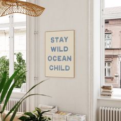 a living room with a plant on the table and a poster that says stay wild ocean child