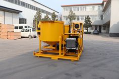 a large yellow machine sitting in the middle of a parking lot next to some buildings