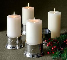 three white candles sitting on top of a table next to christmas decorations and greenery