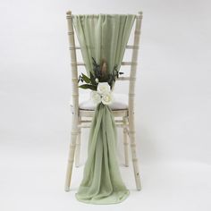 a white chair with a green sash draped over it and flowers on the back seat