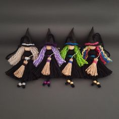 five small witches are lined up in a row on a gray surface, one is wearing a black witch hat and the other has colorful yarn