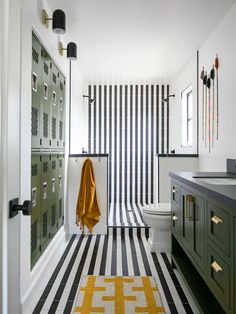 a bathroom with black and white stripes on the floor, green cabinetry, and yellow rug