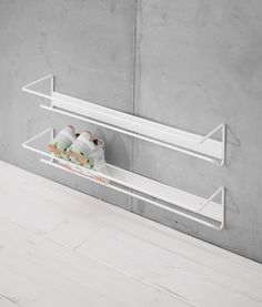 two white shelves with shoes on them against a concrete wall, one shelf holding toilet paper and the other