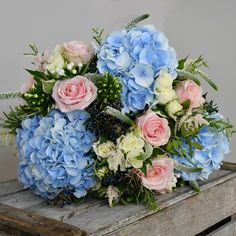 a bouquet of blue and pink flowers sitting on top of a wooden box with greenery