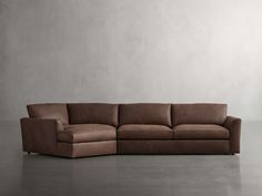 a brown leather couch sitting on top of a floor next to a white wall and lamp