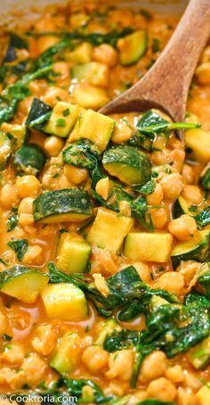 a wooden spoon in a pot filled with chickpeas and zucchini soup