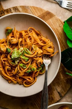 a white bowl filled with pasta on top of a wooden table next to silverware