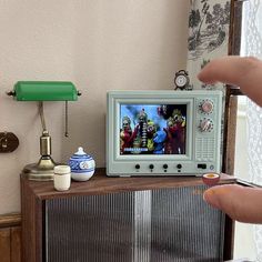 a person pointing at a television on top of a dresser