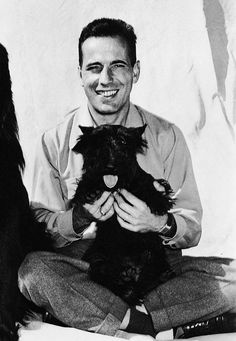 a man sitting on the floor with two dogs in front of him and smiling at the camera