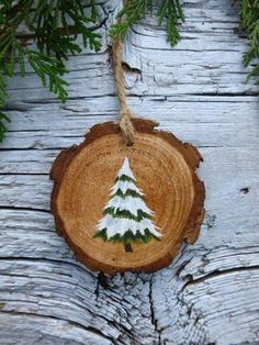 a piece of wood with a painted christmas tree on it hanging from a rope next to some branches