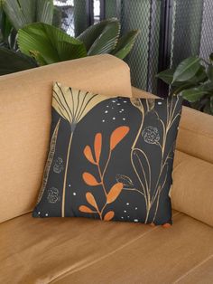 a black and orange pillow sitting on top of a couch next to a plant filled wall