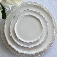 three white plates are stacked on top of each other, with flowers in the background