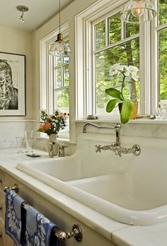 a white sink sitting under two windows next to a window sill with flowers in it