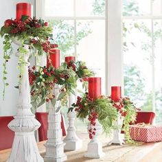 christmas decorations with candles and greenery are displayed in front of a window on a table