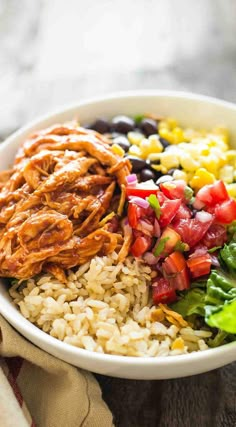 a white bowl filled with rice, beans, corn and chicken salad next to a napkin