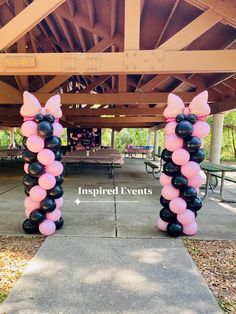 two black and pink balloons in the shape of bows are on display at an outdoor event