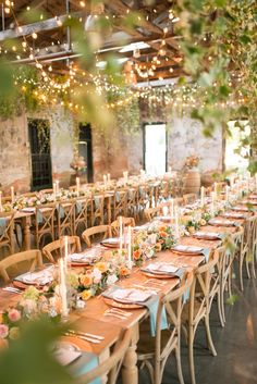 a long table set up with place settings and candles for an outdoor wedding or reception