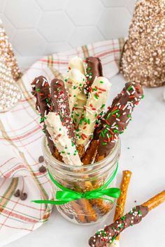 chocolate dipped pretzels in a jar with sprinkles and green ribbon