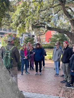 a group of people standing around each other on a brick walkway in front of trees