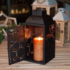 a lit candle sitting inside of a black box on top of a wooden table next to two lanterns