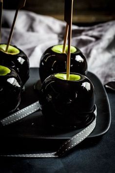 three black vases with green apples in them on a plate next to a white cloth