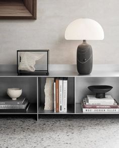 a shelf with books, vase and lamp on it in a room that has gray walls