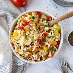 a white bowl filled with pasta salad next to silverware and tomatoes on the side