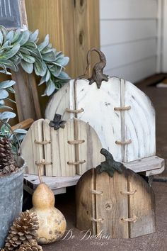 three wooden pumpkins sitting on top of a table next to potted plants and pine cones