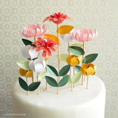 a white cake topped with lots of paper flowers