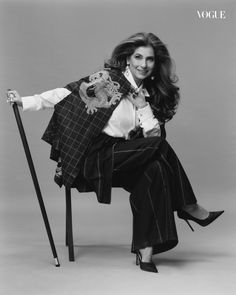 a woman sitting on top of a chair holding a cane and wearing a jacket with an animal