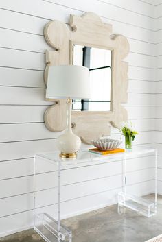 a white table with a lamp and mirror on the wall above it in a room