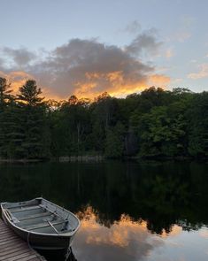 a boat sitting on top of a lake next to a wooden dock with trees in the background