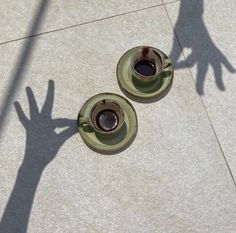 two coffee cups sitting on top of saucers next to each other in front of a person's shadow