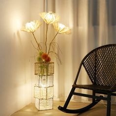 a chair sitting next to a vase with flowers in it and a light on the wall