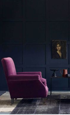 a living room with dark blue walls and purple chairs in front of a painting on the wall