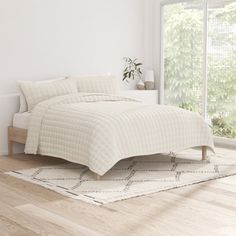 a white bed sitting on top of a hard wood floor next to a large window