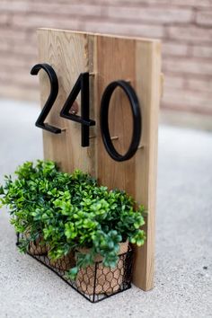 a house number sign sitting on top of a wooden block with plants in the front