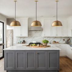 a kitchen with marble counter tops and gold pendant lights hanging over the island in front of it