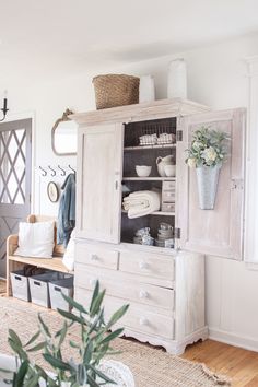 a white cabinet with baskets on top of it next to a plant in a vase