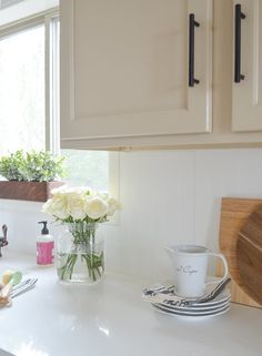 a white kitchen counter with flowers in a vase and plates on the counter next to it