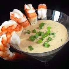 a bowl filled with shrimp and dip surrounded by scallops on a black surface