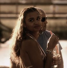 two women standing next to each other holding drinks and looking at something in the distance