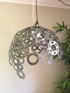 a light fixture made out of gears hanging from a ceiling in front of a potted plant