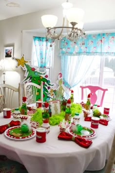 the table is set for christmas dinner with red and green dishes, cups, candy canes, santa's helper hats