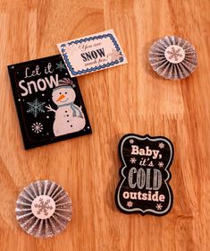 baby it's cold outside magnets and badges on a wooden table with snowflakes